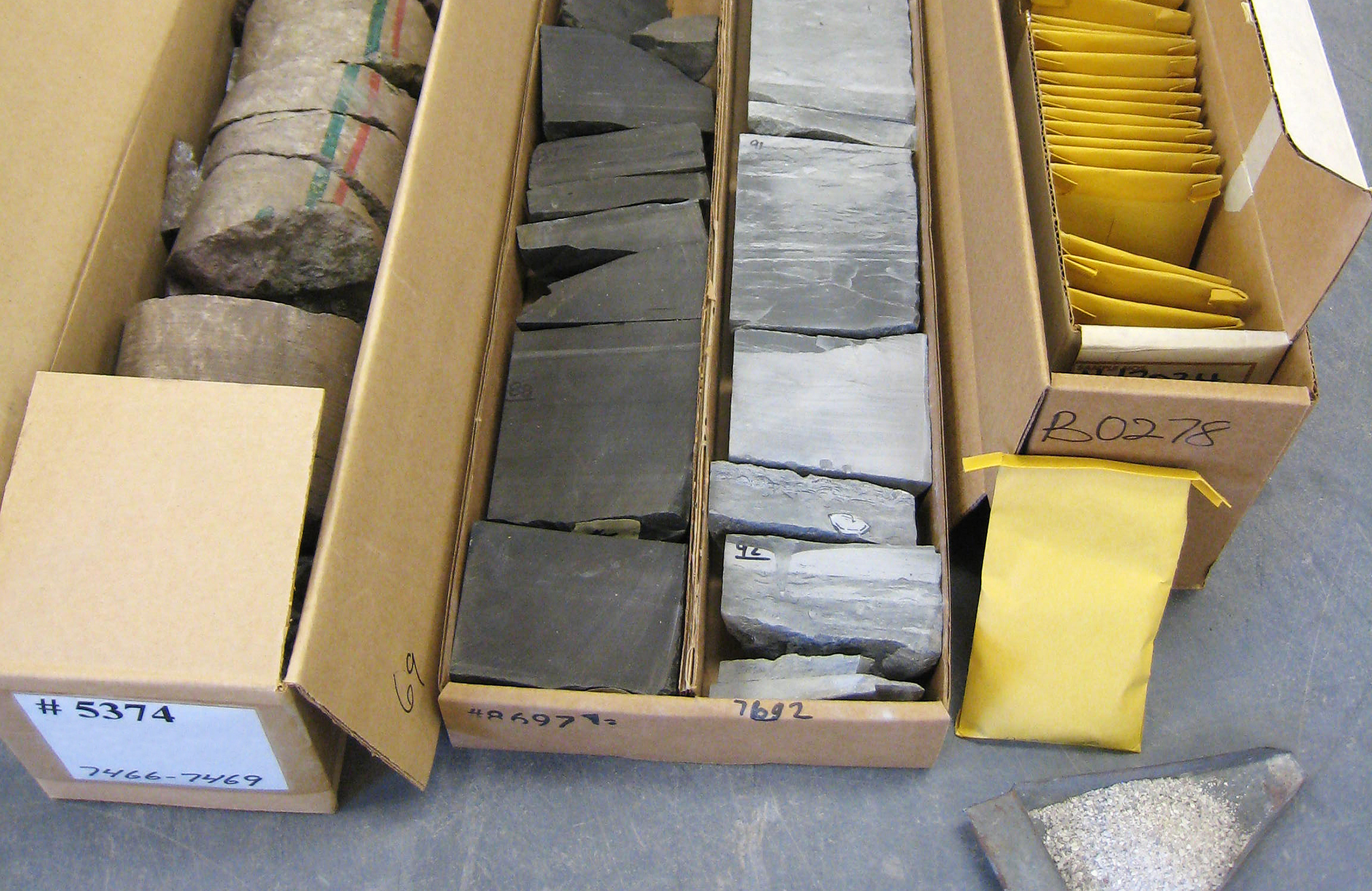 Three long cardboard boxes filled with small envelopes and chunks of rock.