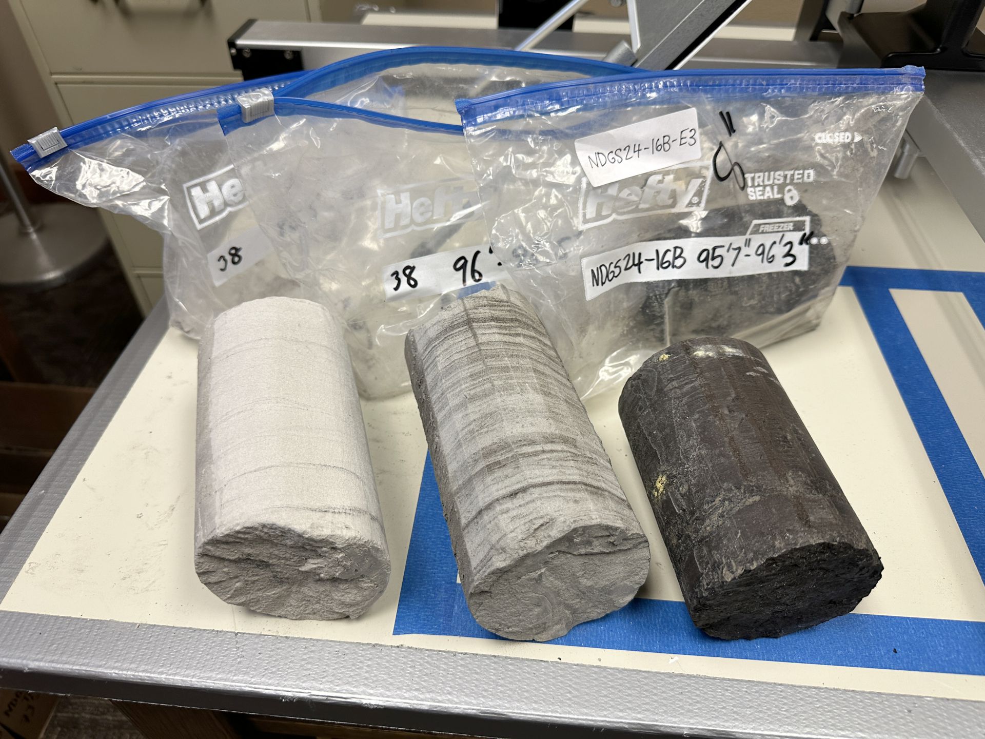 Set of three rock cores laying on a table beside marked, plastic bags.