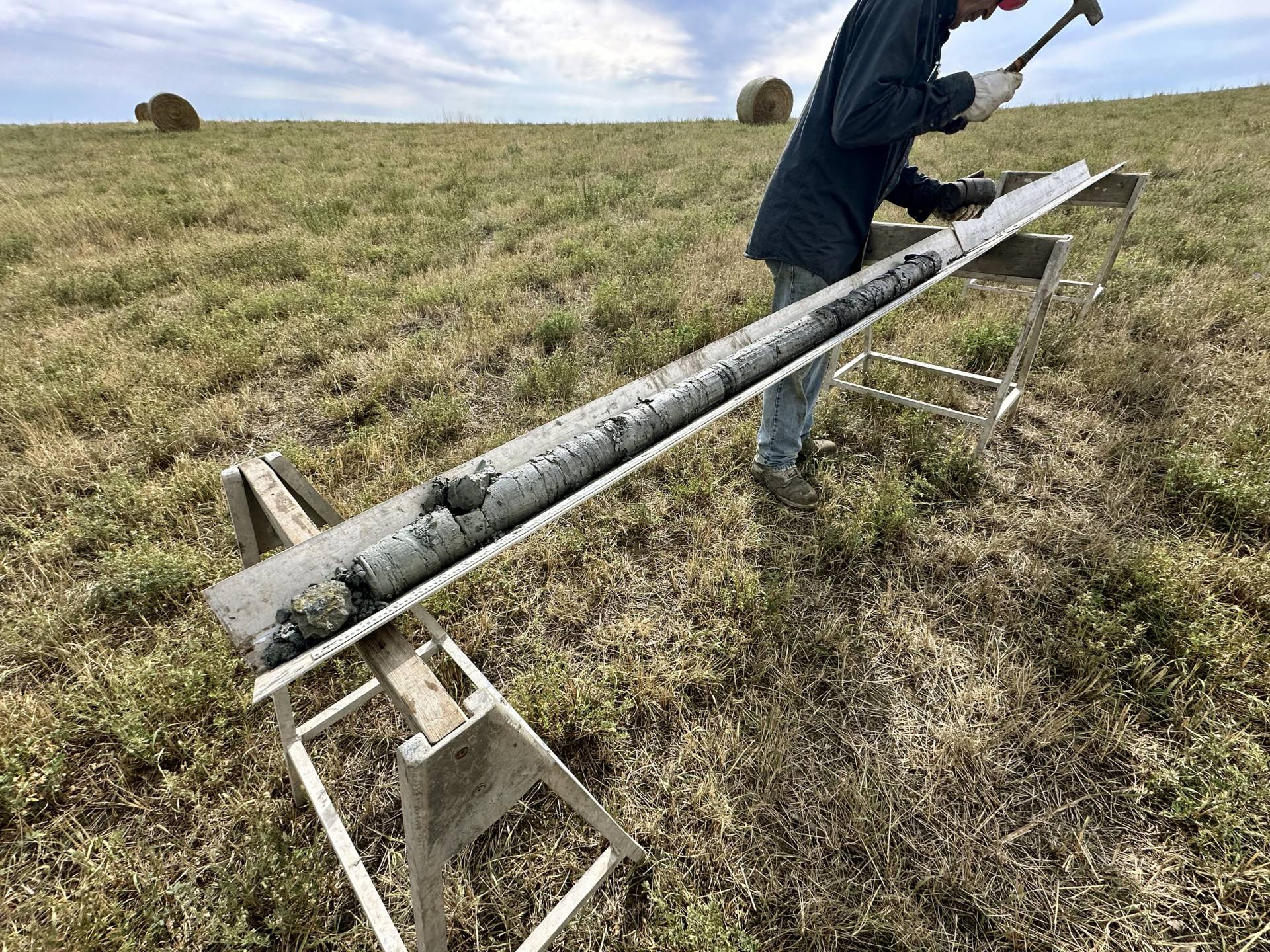 A photo of a man standing in a field holding a pick axe and a rock sample.