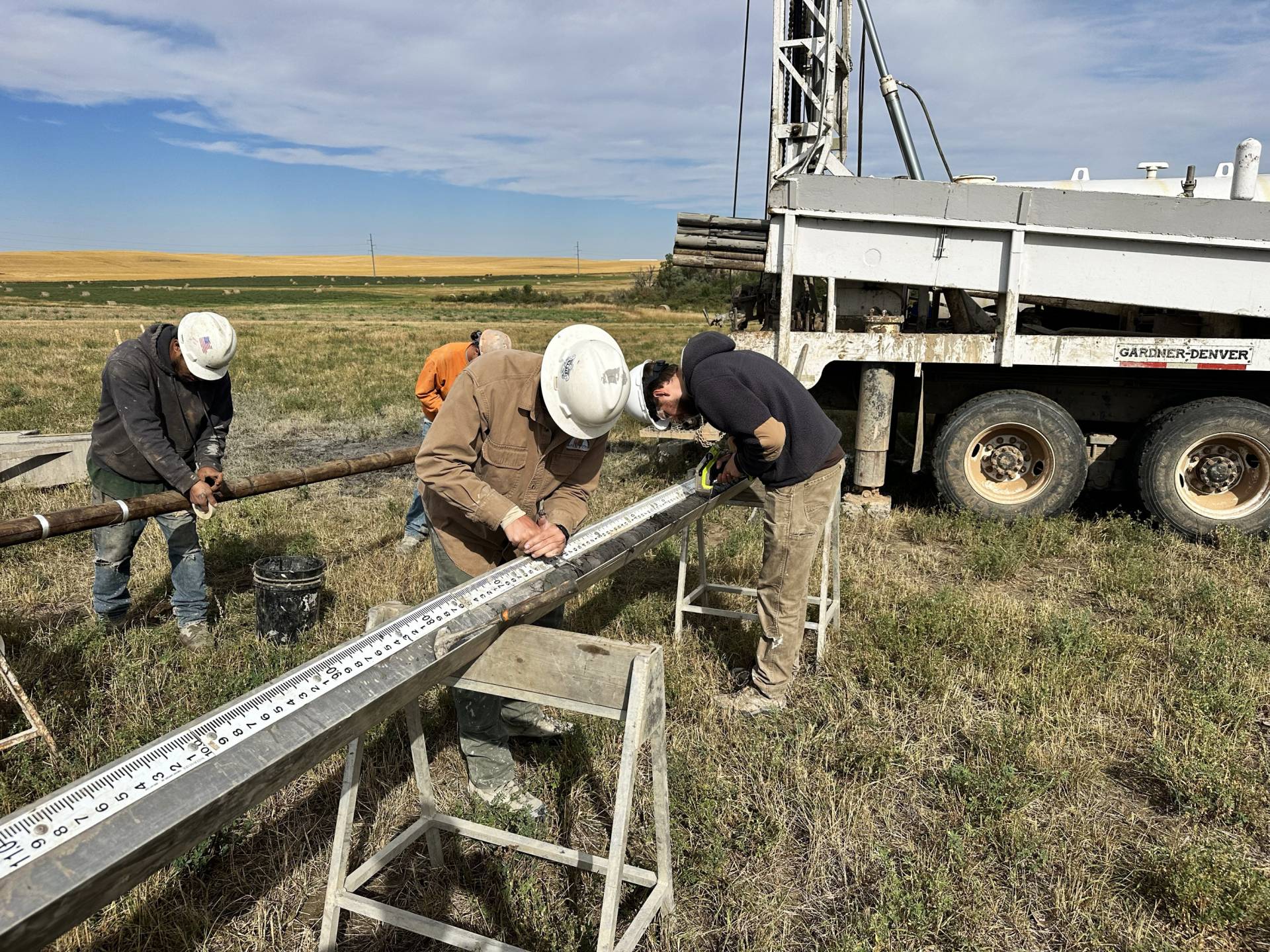 A photo of four men wearing hard hats standing in a field next to a truck.