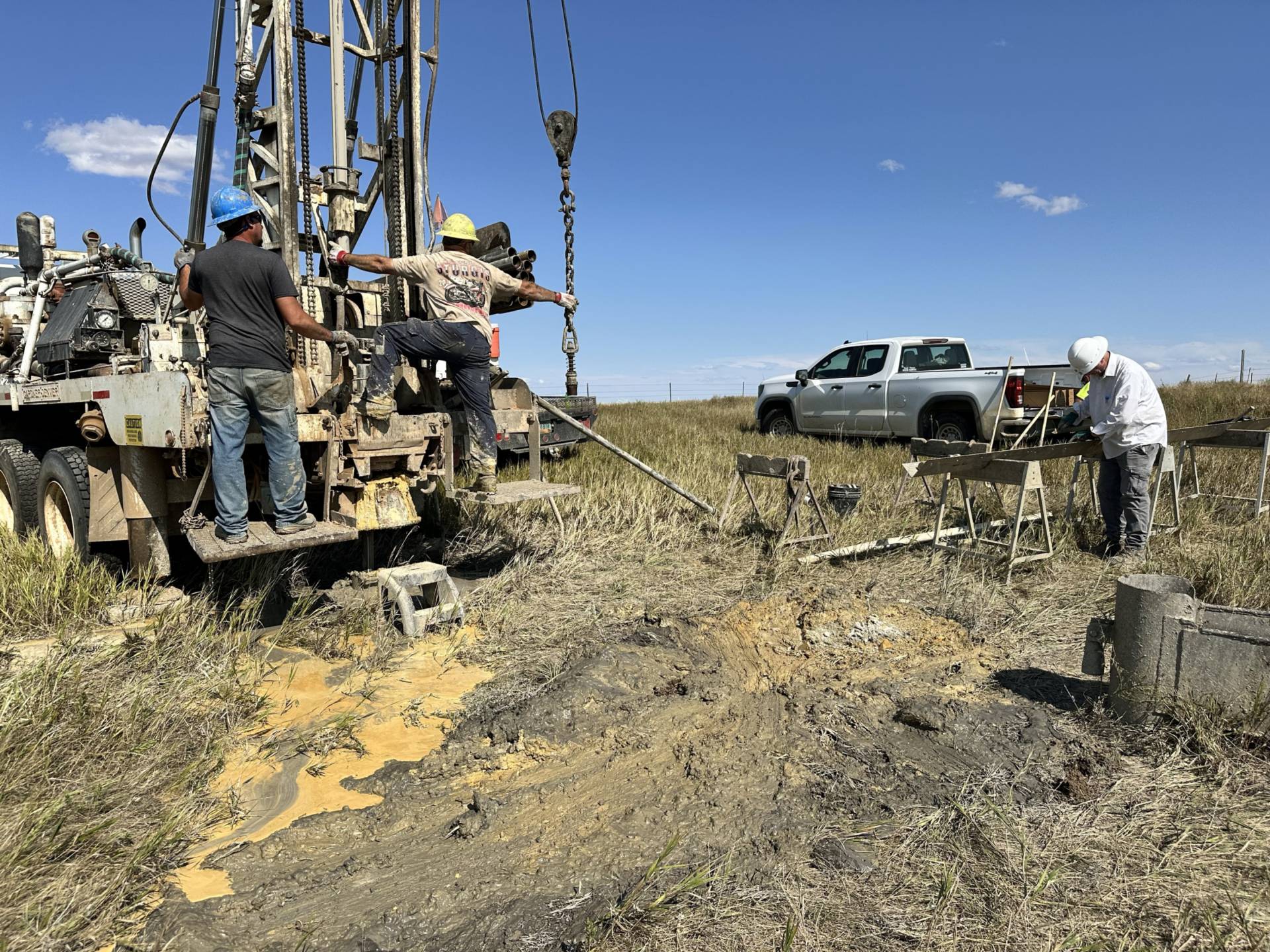 A photo of three men in hard hats next to a drilling truck and orange colored mud.